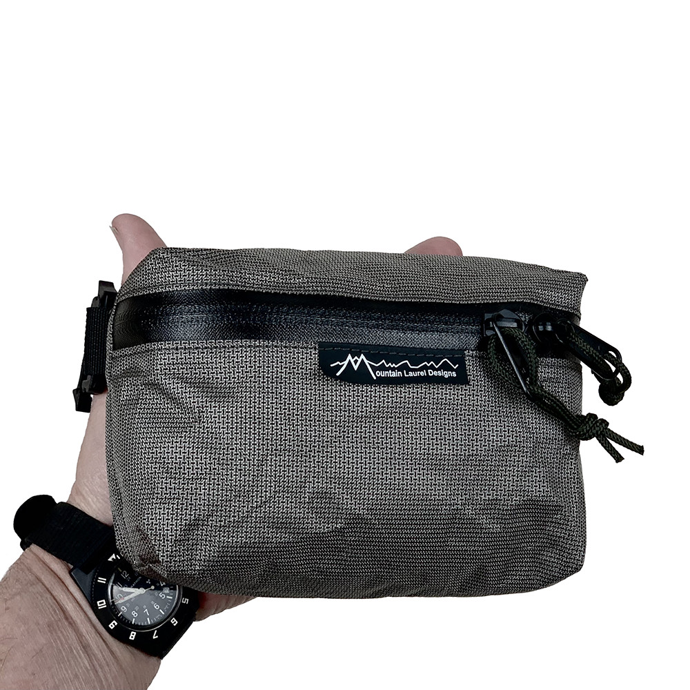 A man holds a MLD Pack Pocket in his hand. You can only see the tips of his thumb and forefinger.